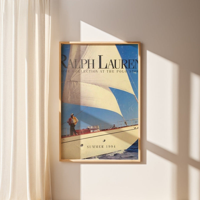 Vintage sailboat poster Ralph Lauren style Summer 1994 in wooden frame on beige wall with sunlight shadows.