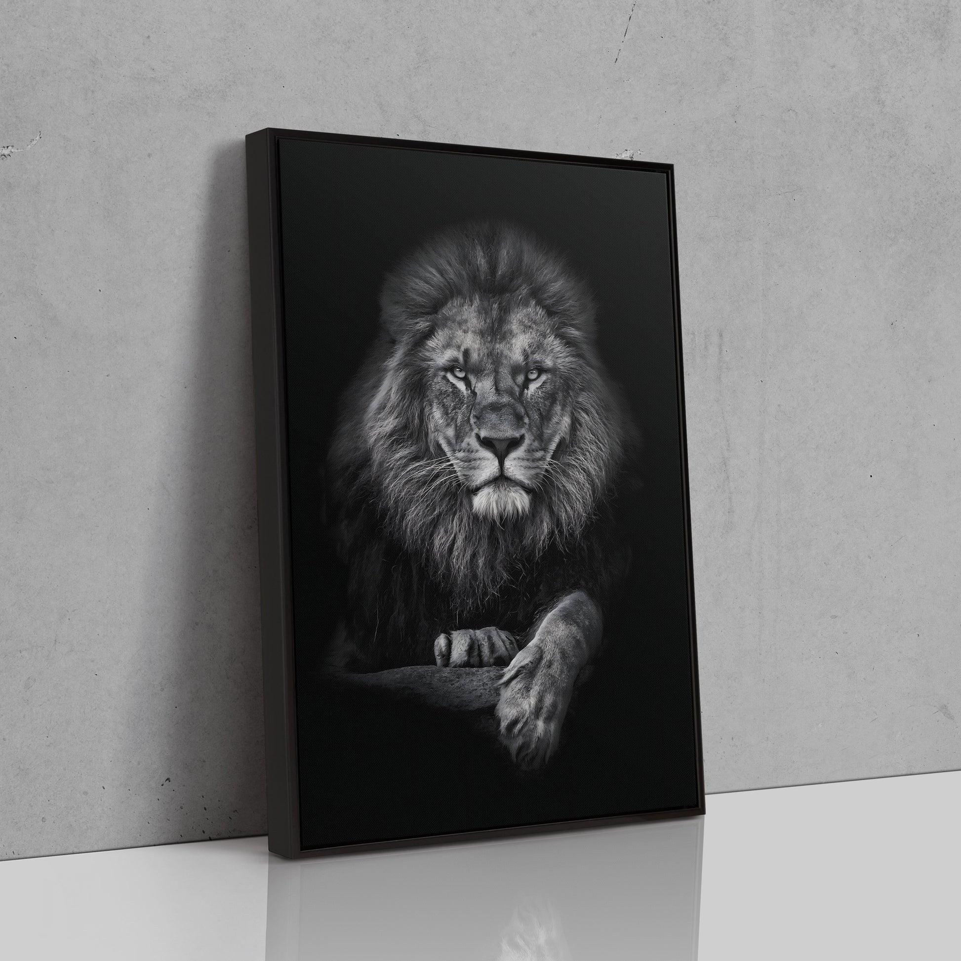 Framed monochrome lion canvas leaning against a concrete wall, angled view showing the black floater frame