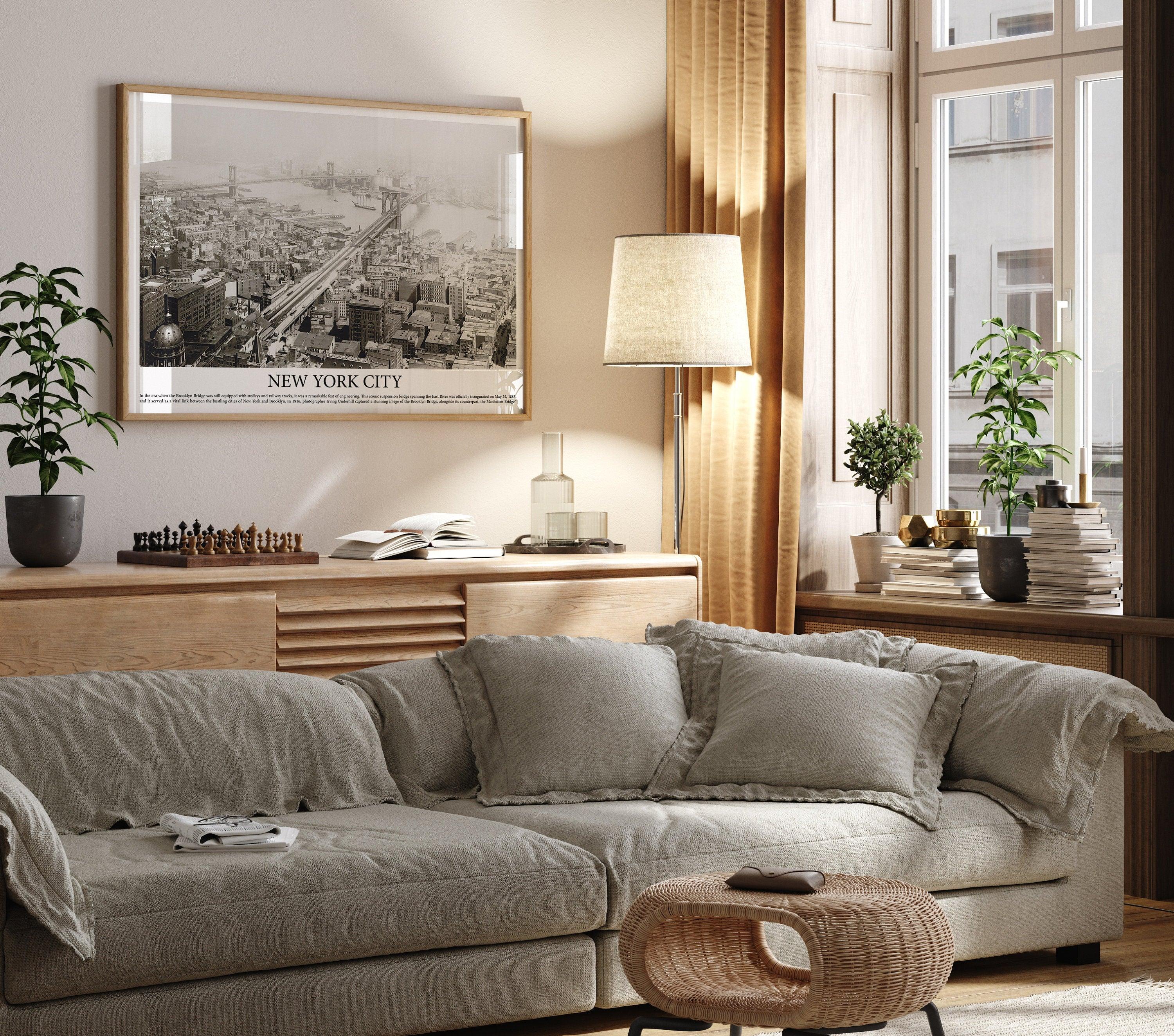 Oak framed vintage Brooklyn Bridge aerial photo on a warm beige living room wall above a linen sofa
