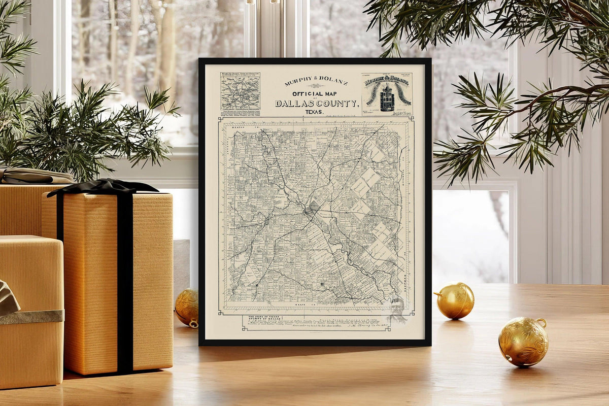 Framed antique Dallas County Texas map print resting on a table beside gold ornaments and wrapped gifts